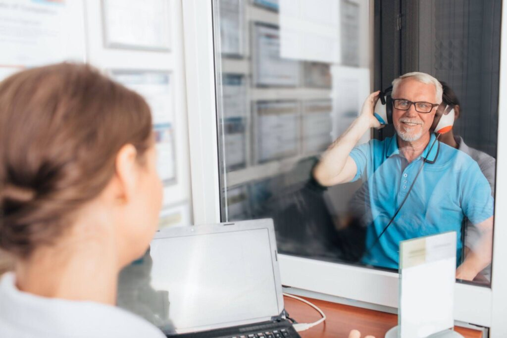 An audiologist testing a man‘s hearing in a booth